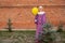 Street cosplay for halloween, carnival or party. A guy in a clown or mime costume with a yellow ball near a small green Christmas
