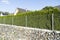 Street fence made of steel mesh, concrete is installed, pebble stones are below. Thuja green hedge grows next to the fence
