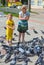 On the street, girls feed pigeons seeds.