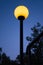 Street lamp with bright yellow light against the evening deep blue sky. Bright sphere shape outdoor lamp in dusk.