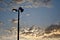 Street lamp under a blue cloudy sky during a beautiful sunset with a plane flying through it