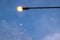 Street light with black post and illuminated orange light looking from below against blue cloudy sky.