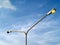 street light pole with yellow orange light bulb against cloudy blue sky