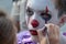 Street makeup in the style of Halloween. A female hand with a brush paints the face of a teenager boy. The image of a clown or