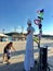 A street performer on stilts making a balloon animal for a small child with his mother beside him