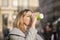 Street portrait of a beautiful young and round-faced woman 25-30 years old with blonde hair in a gray hoodie, who drinks coffee fr