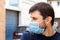 Street portrait of a frowning caucasian man in protective blue medical mask in period of pandemic coronavirus covid-19