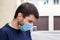 Street portrait of a frowning caucasian man in protective blue medical mask in period of pandemic coronavirus covid-19