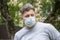 Street portrait of a man 40-45 years old in a medical mask against the background of nature.A serious look is directed to the side