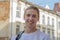 Street portrait of a smiling young guy 20-25 years old with a backpack on his shoulder against the background of old urban archite