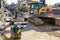 Street reconstruction site with workers, excavators, vibratory plate compactors and other machinery