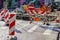 Street repair site with red and white striped warning signs, barriers, temporary metal fence