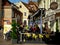 Street scene in morning sunlight with cafe terrace and tourist having coffee