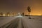 Street through snow in winter with city lights on horizon