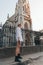 Street style photo, attractive blonde girl in white shirt and black boots stands in front of the old church