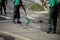 Street sweeper cleaning city sidewalk with water from a hose and a plastic broom - blue collar jobs