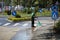 Street sweeper cleaning city sidewalk with water from a hose and a plastic broom - blue collar jobs