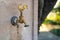 Street tap with golden metal cock and running water, set on old stone platform. Outdoors