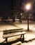 The streetlamp and a bench covered with snow in the park at night