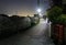 Streetlights on empty road by dark greenhouses at night