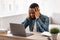 Stressed Black Businessman Having Headache Sitting At Workplace In Office