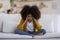 Stressed black little girl sitting on couch at home