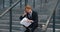 Stressed businessman with business papers in his hands sits on the steps of an office building. Sad overworked redhead