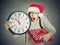 Stressed in a hurry woman wearing santa claus hat holding clock gift box