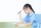 Stressed little girl in school uniform sitting at desk isolated over white background. Schoolgirl unhappy doing homework. Student