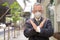 Stressed mature Japanese businessman with mask and face shield showing stop gesture in the city