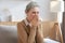 Stressed middle aged woman sit on sofa in living room, lost in thought