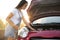 Stressed pregnant woman fixing broken car on city street