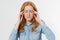 Stressed red hair woman portrait having a migraine headache holding her head in pain and stress isolated over white background