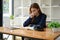 A stressed and unwell Asian woman focuses on reading a book while sitting at a table