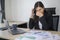 Stressed young business woman working on laptop with documents in modern office, workload concept