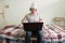 Stressed young man with tin foil hat using laptop and looking angry in the bedroom