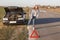 Stressful young woman driver hitchhikes and stops cars, asks for help as have problem with brocken car, uses red triangle sign to