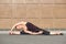 Stretching gymnast woman doing split, twine in brown urban wall background