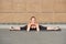 Stretching gymnast woman doing split, twine in brown urban wall background