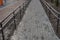 Stretching into perspective sidewalk with rectangular tiles and black metal railing fence leading to the newly built sports ground