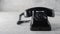 A strict vintage black telephone with a long twisted cord to the handset, on a wooden table with white shabby paint.