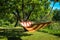 A striped hammock between two trees in a sunny green garden.