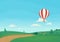 Striped hot air balloon flying over rural landscape with green meadows, trees, bushes, dirt road and forest with clouds and blue