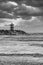 Striped lighthouse during a vibrant sunset. Water hits the black boulders in waves. black and white, dramatic sky. Scheveningen,