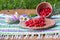 On a striped napkin stands wooden bowl and a cup with wild strawberries near the beautiful flowers.