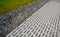 Striped white mosaic tile marble. gray stripes sidewalk with walls of gabion baskets around. gray metal garden gate. low fencing f