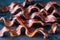 Strips of crispy maple pepper bacon on a black slate board.