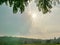 Strong afternoon sunlight in summer shining through cloudy sky onto hills, green leaves, and the ground below