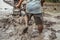 Strong asian farmer driving tiller tractor in muddy field, detail of male farmer walking barefoot in deep mud