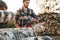 Strong bearded lumberjack in plaid shirt sawing tree with chainsaw